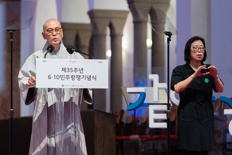 민주화운동기념사업회 지선 이사장(좌)이 기념식에서 경과보고를 하는 모습과 이를 수어통역사(우)가 통역하고 있다.